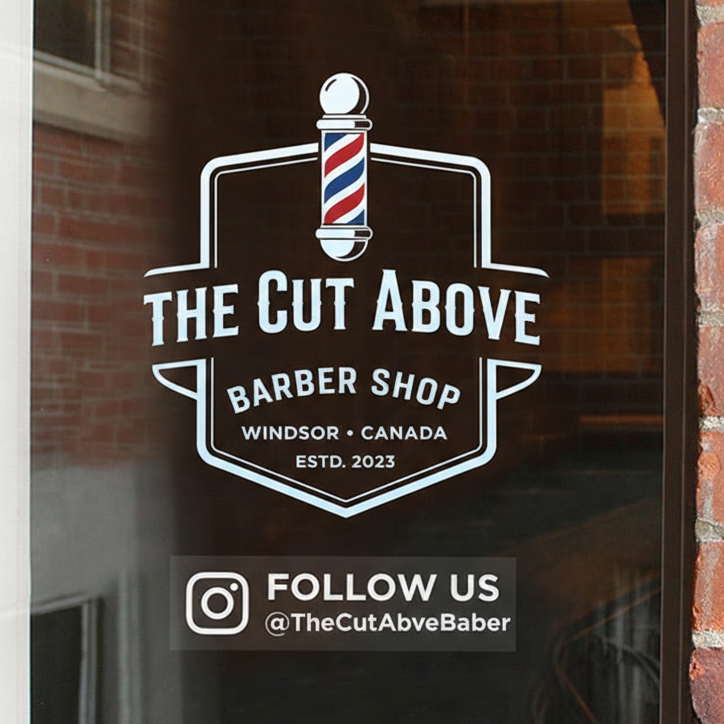Logo of 'The Cut Above Barber Shop' on a glass door with brick wall background.
